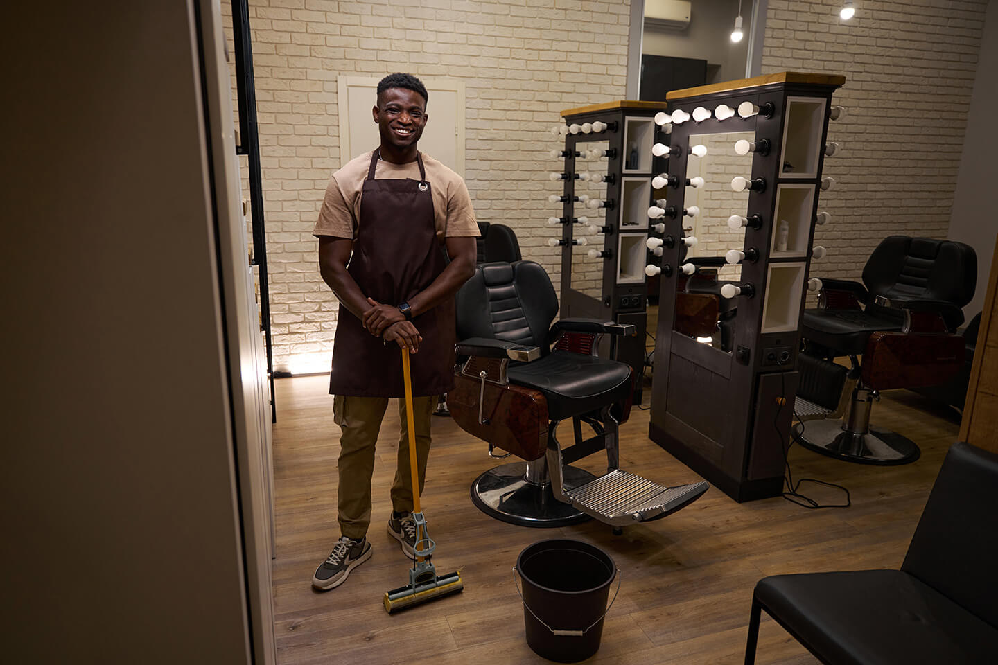Barber in a work apron cleans in a barbershop