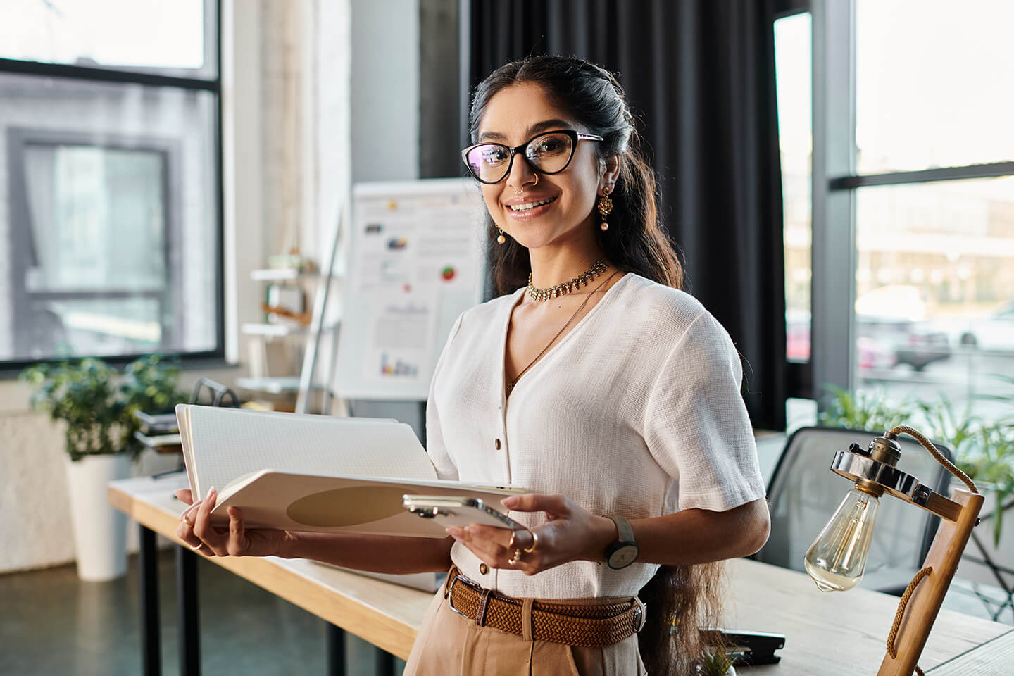 A professional woman stands by her desk holding business documents.